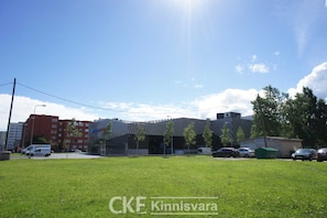 A grassy area with a building in the background, a parking lot with several cars, and a clear sky.