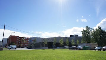Une zone herbeuse avec un bâtiment en arrière-plan, un parking avec plusieurs voitures et un ciel dégagé.