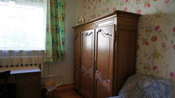 Une pièce avec une armoire en bois, un lit recouvert d’une couverture à motifs, une fenêtre avec des rideaux et un radiateur.