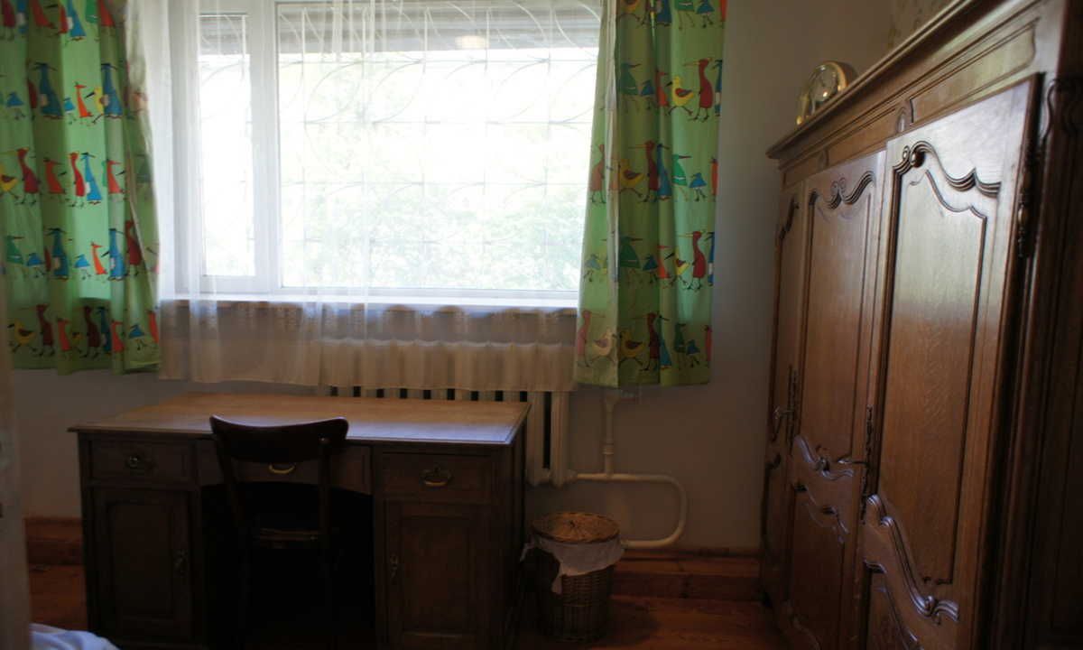 Habitació amb escriptori de fusta, una cadira, un armari i una finestra amb cortines.