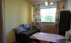 Una habitación pequeña y acogedora con una cama, una mesa y una silla. Cuenta con una ventana con cortinas, un radiador y una puerta.