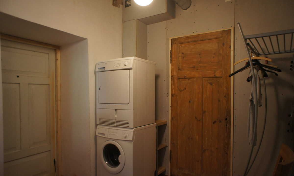 Un cuarto de lavandería con electrodomésticos apilados, una puerta de madera y un tendedero.