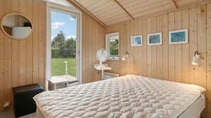 A bedroom with a large bed, a round mirror, a fan, and a window with a view of a garden.
