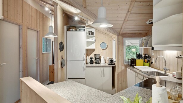 A compact kitchen with wooden walls, a white refrigerator, a coffee maker, and a sink.