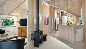 A modern kitchen with a central wood-burning stove, wooden cabinetry, and a dining area with a table and chairs.