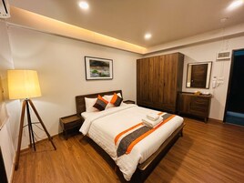Quarto de hotel com cama, mesa de cabeceira, abajur, guarda-roupa e um quadro na parede.