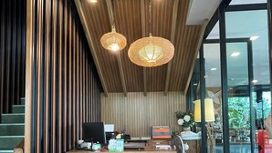 A modern interior with a wooden slatted wall, a desk with chairs, and a staircase. - The Bedrooms Maeklong Service Apartment (Samut Songkhram)