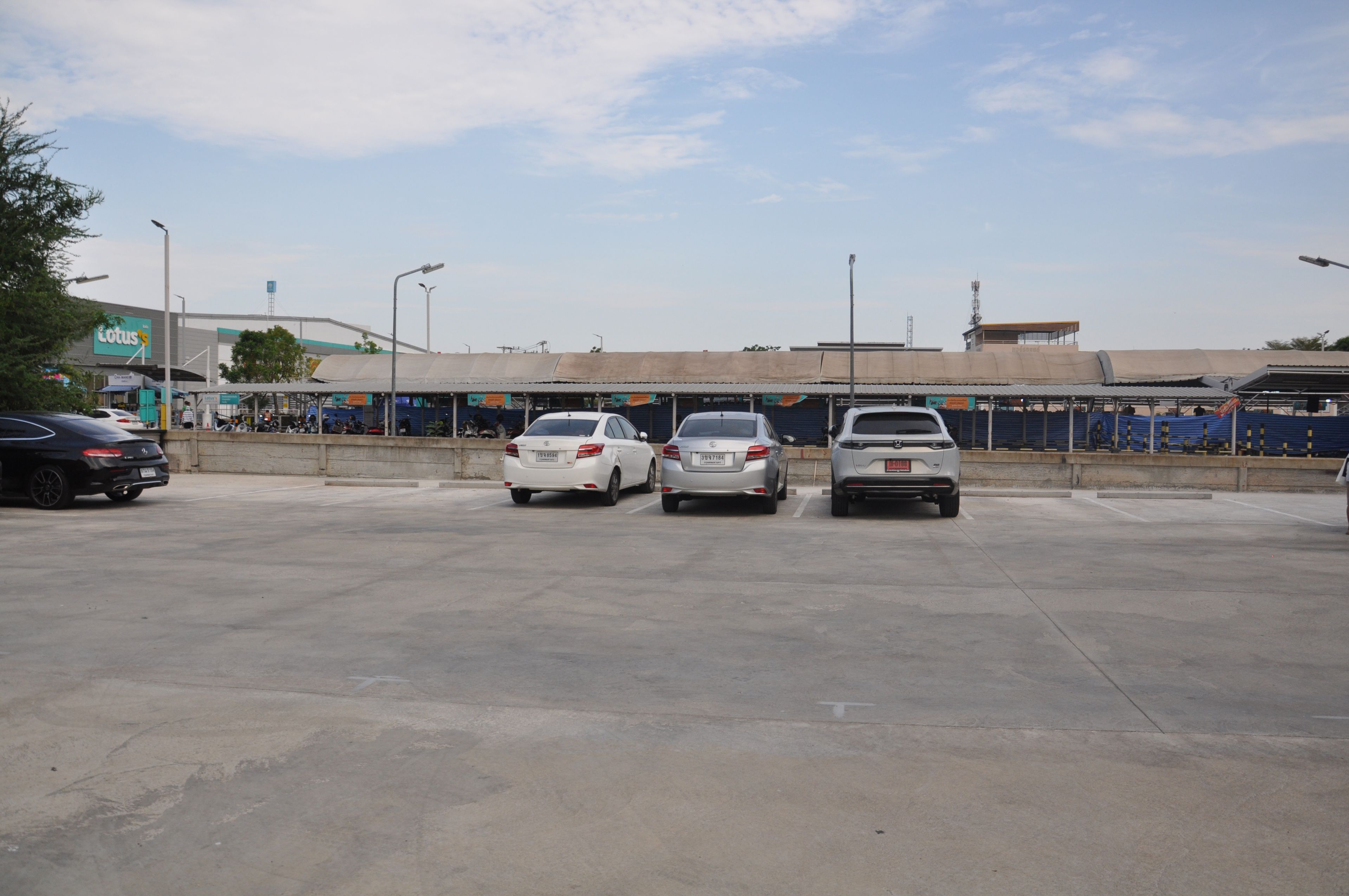 A parking lot with several cars parked, a building with a sign that reads 'Lotus,' and a clear sky.
