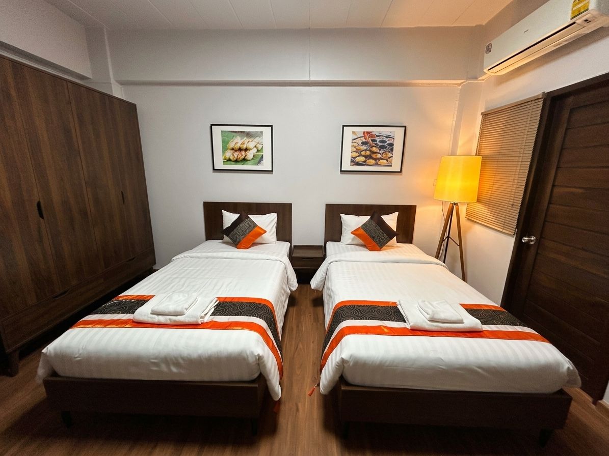 A hotel room with two beds, a wardrobe, a lamp, and wall art.