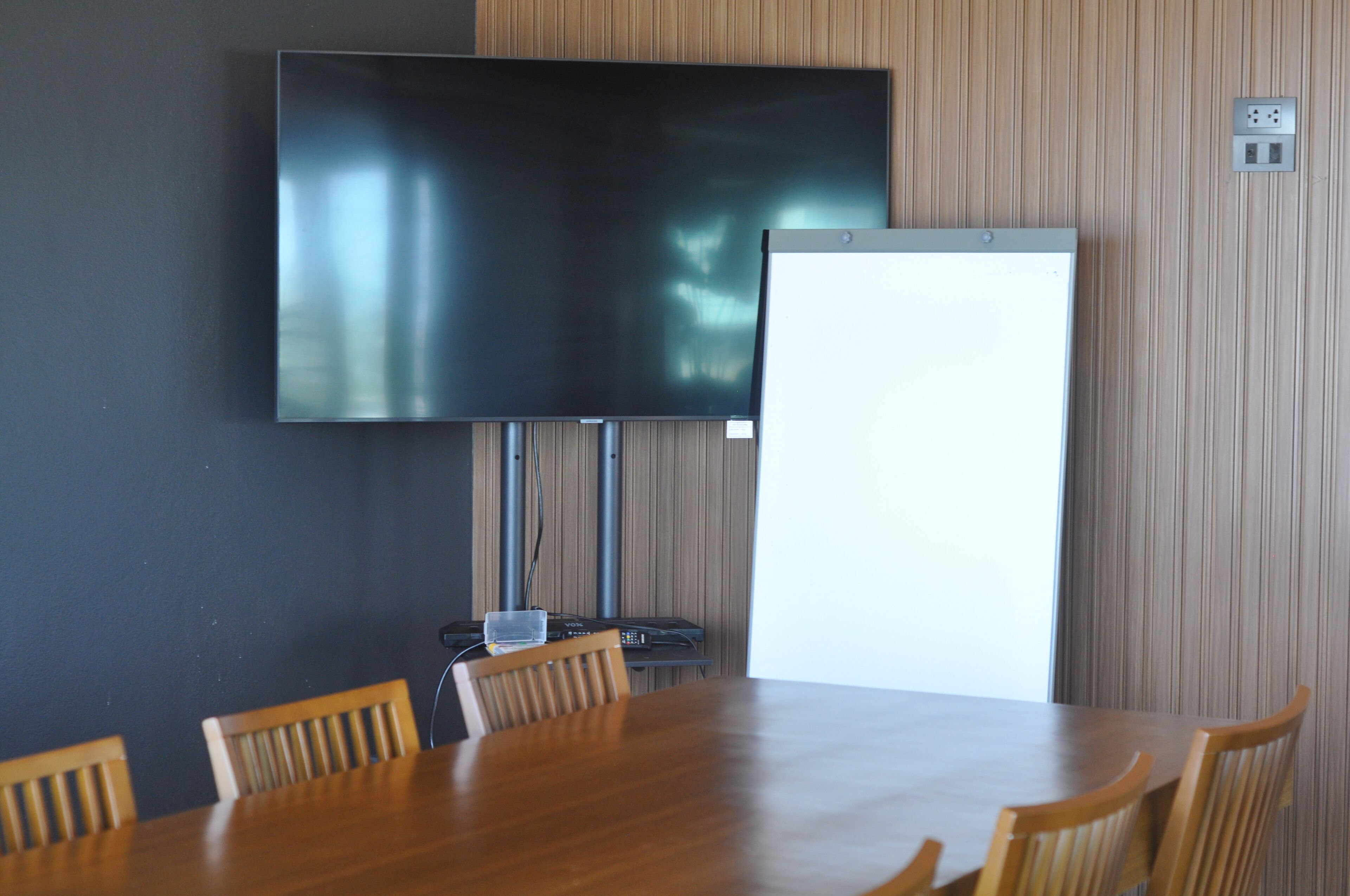 A conference room with a large table, four chairs, a flat-screen TV, and a whiteboard.