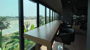 A long table with chairs in a room with large windows. - The Bedrooms Maeklong Service Apartment (Samut Songkhram)