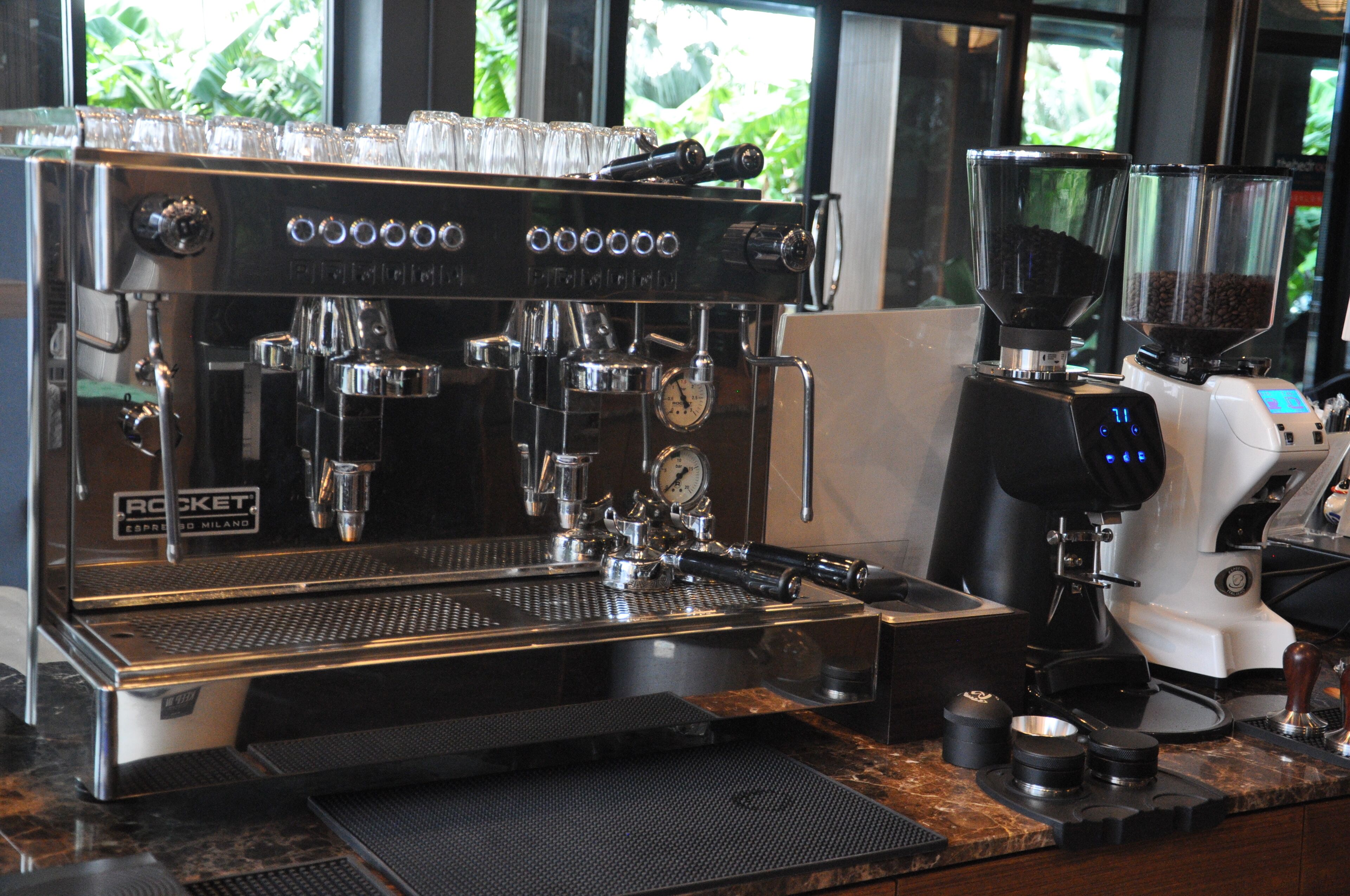 Una máquina de espresso comercial con varios dispensadores de café y un molinillo, sobre una encimera de mármol.