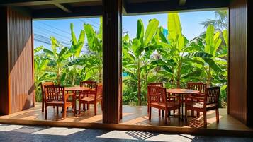 Un área de estar al aire libre con muebles de madera y vistas a exuberantes plantas de plátano.