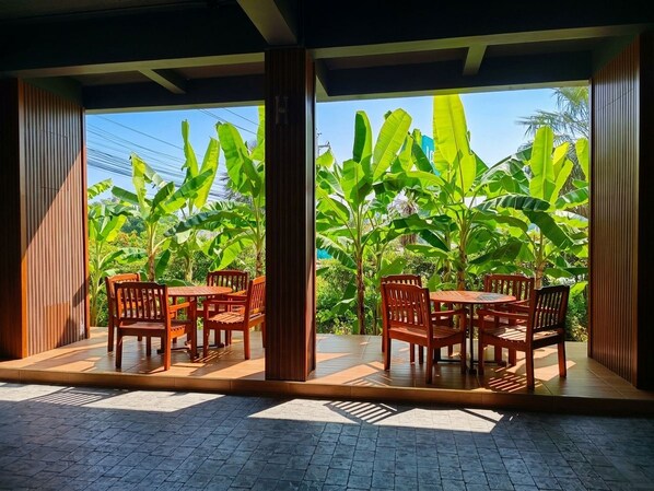 Un área de estar al aire libre con muebles de madera y vistas a exuberantes plantas de plátano.