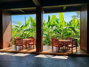 An outdoor seating area with wooden furniture and a view of lush banana plants. - The Bedrooms Maeklong Service Apartment (Samut Songkhram)