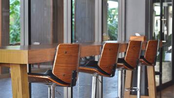A row of wooden chairs with metal legs, arranged in front of a long wooden table in a modern interior space with large windows.