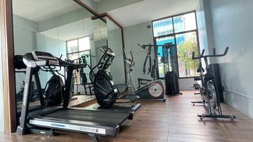A gym with a treadmill, elliptical, and stationary bike, large windows, and a mirror.