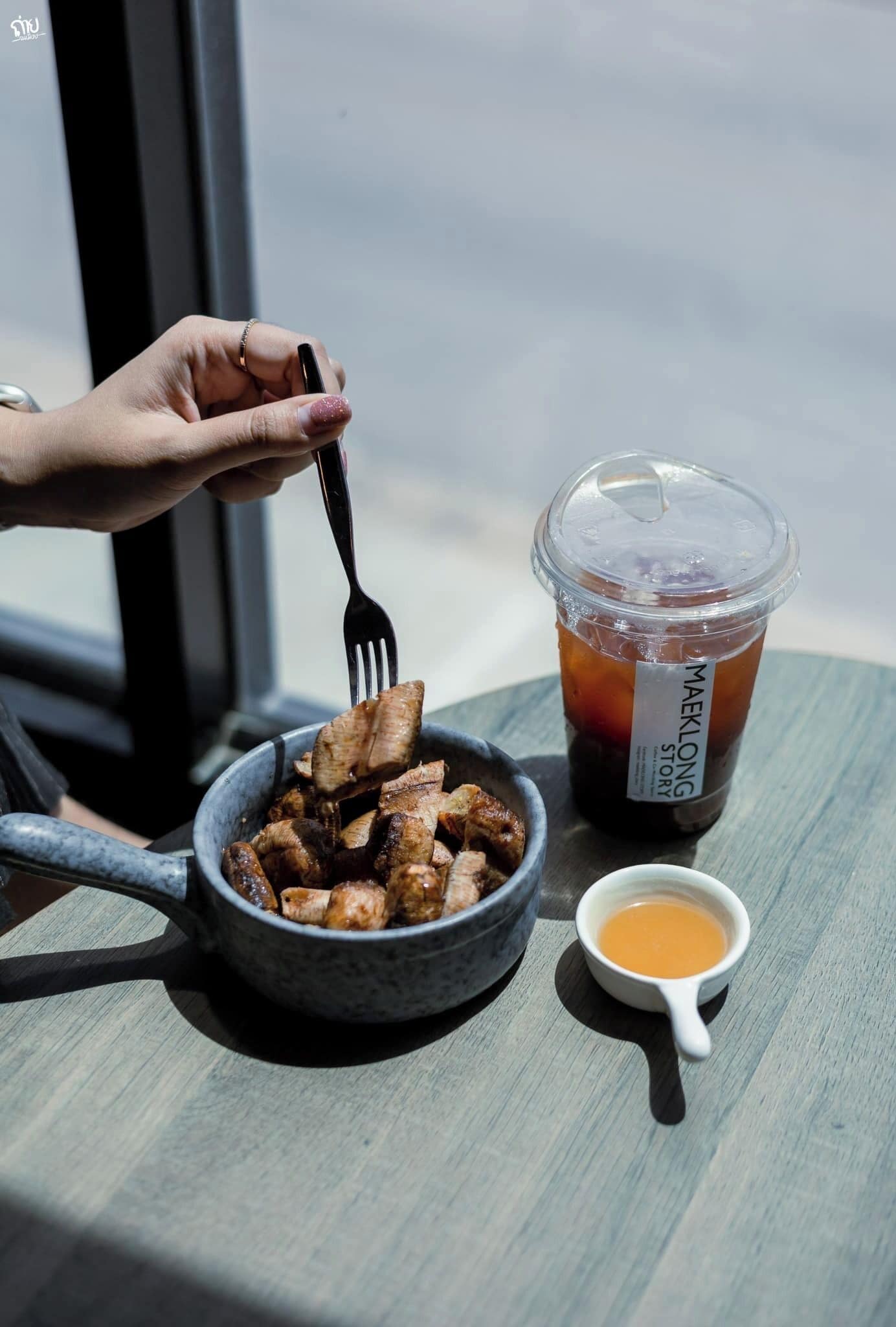 Una comida con un plato de alimentos, una bebida en vaso de plástico y un recipiente pequeño con salsa sobre una mesa cerca de una ventana.