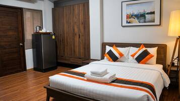 A hotel room with a bed, a wardrobe, a refrigerator, and a painting on the wall.