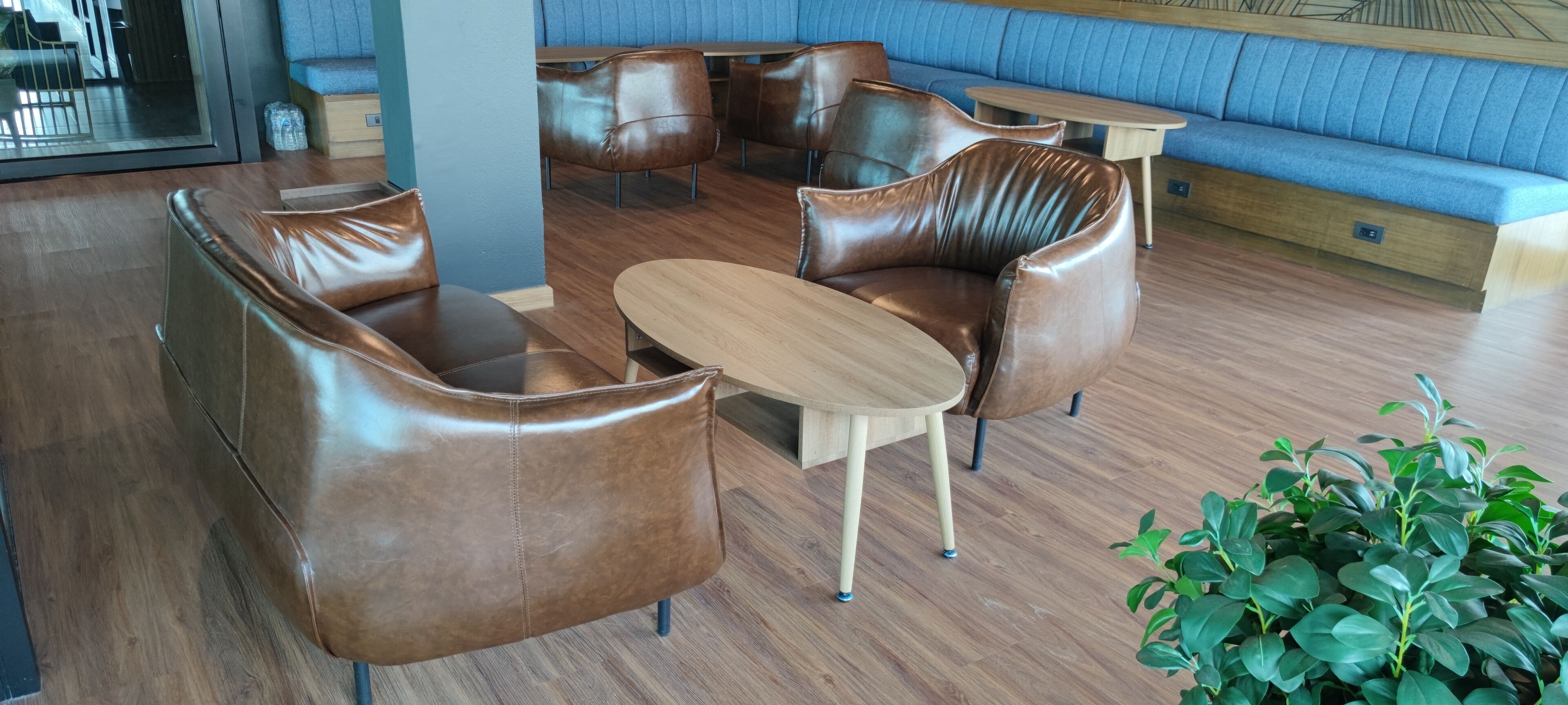A modern lounge area with leather sofas and a wooden table, featuring a blue cushioned bench in the background.
