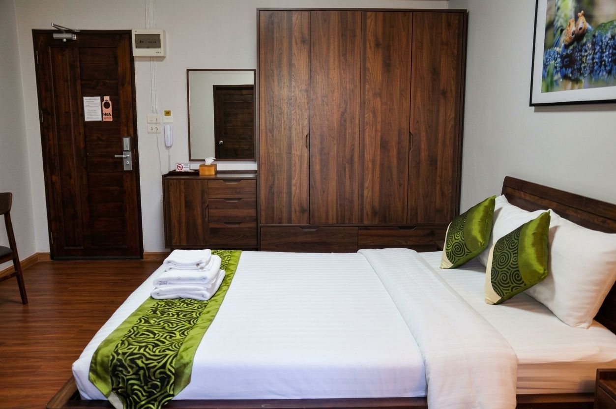 A hotel room with a bed, a wardrobe, a mirror, and a painting on the wall.