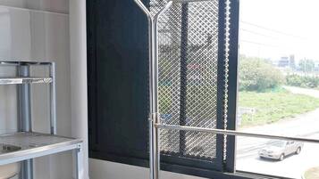 Esquina de una habitación con un estante metálico, un recipiente azul y una ventana que da a la calle.
