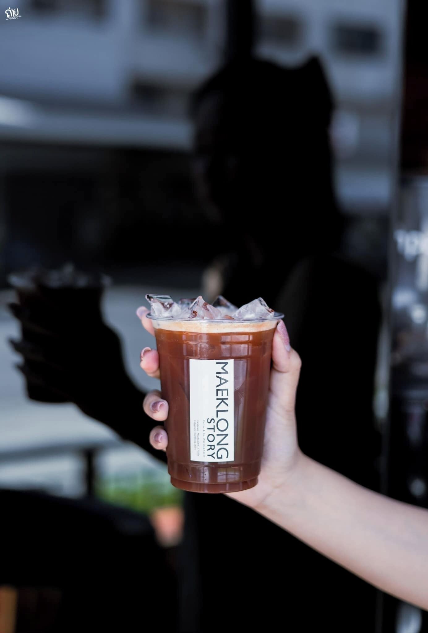 A hand holding a Maeklong Story drink with a label.