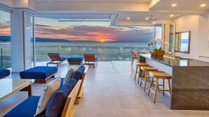 A modern interior with a balcony overlooking a sunset over water.