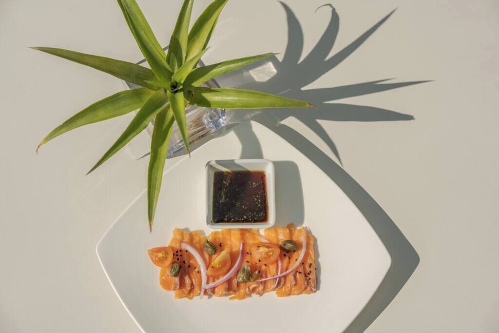 En vit tallrik med laxsashimi, en liten skål med sås och en grön växt.