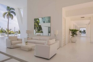 Un interior moderno con un juego de sofá blanco, un espejo grande y vistas a palmeras.