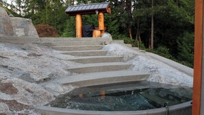 Una escalera de piedra conduce a un área de aguas termales, con una estructura de madera al fondo.