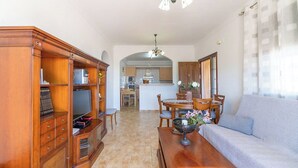 A living room with a sofa, a wooden cabinet, a television, and a dining area with chairs and a table. - Villa Medina Torrox by Ruralidays (Málaga)