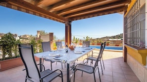 An outdoor patio with a table set for dining, chairs, a pool, and a view of the surrounding area. - Villa Medina Torrox by Ruralidays (Málaga)