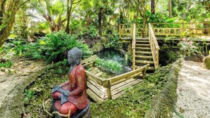 A serene garden with a Buddha statue, a small pond, and a wooden bridge. - The Romantic Bird House | A Storybook Garden Retreat (Homestead)