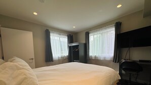 A hotel room with a large bed, a desk with a chair, a wardrobe, and a TV mounted on the wall. - Kitimat River Motel & Suites (Kitimat)