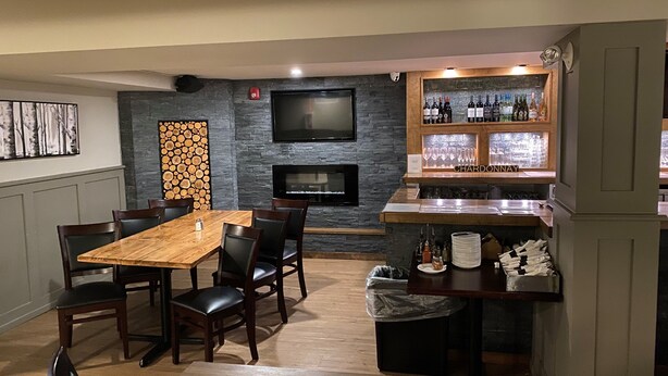 A dining area with a wooden table and chairs, a stone wall with a fireplace, and a bar with bottles and glasses. - Kitimat River Motel & Suites (Kitimat)