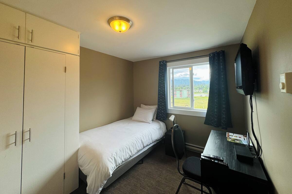 A small, single-bed room with a desk, chair, and a television.