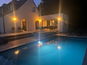 Una casa moderna con piscina, area salotto esterna e patio ben illuminato.