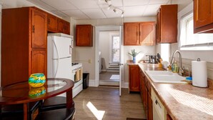A compact kitchen with wooden cabinets, a white refrigerator, a stove, a sink, and a dining area with a glass table and chairs. - *5 Min to WVU*Smart TV*2 Full Kitchen*W/D (Morgantown)