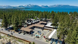 An aerial view of a resort with a swimming pool, parking area, and buildings surrounded by dense forest and mountains. - Blue Jay Lodge (South Lake Tahoe)