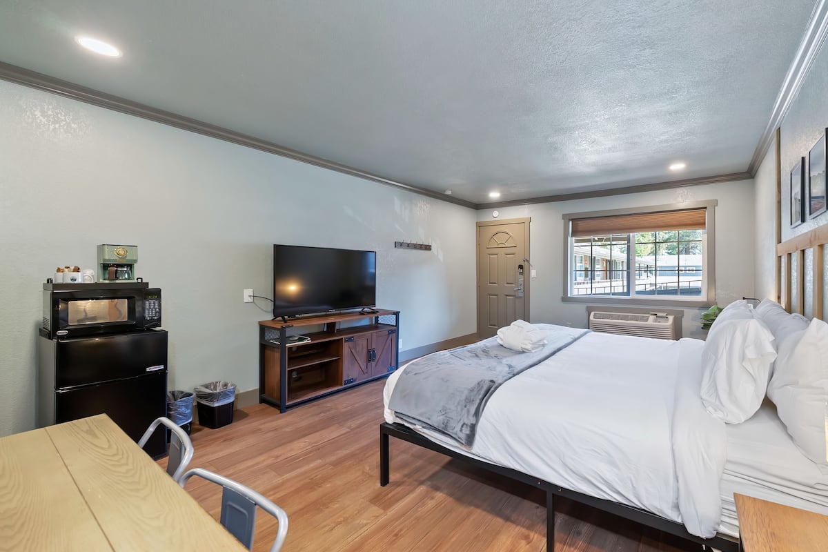 A compact hotel room with a bed, a TV, a small kitchenette, and a window with a view.