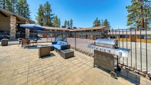 An outdoor patio with seating, a grill, and a building with stone pillars and a covered area. - Blue Jay Lodge (South Lake Tahoe)