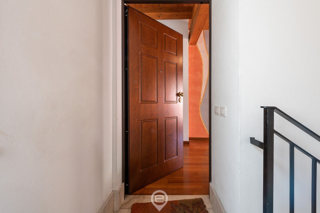 A wooden door leading to a hallway with a carpeted floor and a black railing.