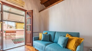 A room with a teal sofa, wooden flooring, and a sliding glass door leading to an outdoor area with a table and chairs. - La Terrazza della Marina (Cagliari)