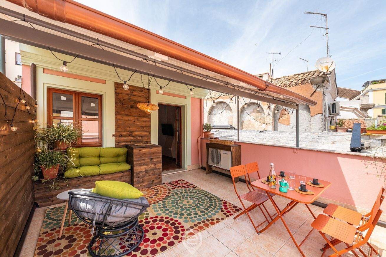 Une agréable terrasse extérieure avec un banc en bois, un tapis coloré et une table avec des chaises.