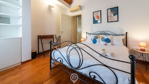 A bedroom with a metal bed frame, a wooden desk, and a chair. There is a door leading to another room, and two wall-mounted lamps. - La Terrazza della Marina (Cagliari)