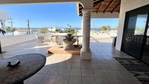 Un patio cubierto con vistas al mar, una fuente de piedra y un suelo de baldosas.