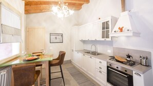 A kitchen with white cabinets, a wooden ceiling, a chandelier, and a dining area with chairs and a table.