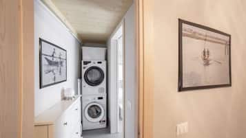 Une buanderie équipée de machines à laver et de sèche-linge superposés, d’une armoire blanche et de tableaux encadrés accrochés aux murs.