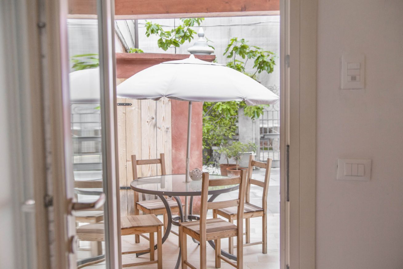En uteplats med ett runt bord och trästolar, ett parasoll och en träpergola.